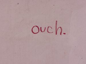 "ouch." written in red on a pink wall